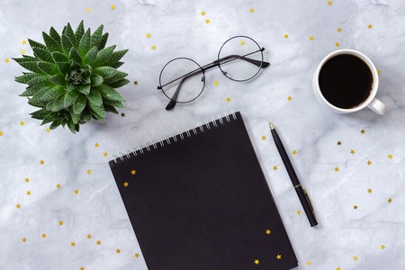 Office or home table desk. Black notepad, pen, cup of coffee, succulent, glasses and gold stars on marble background Concept stylish workplace Flat lay Top view Mockup.の写真素材