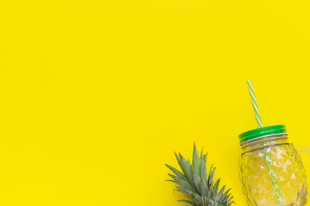 Empty glass jar with green leaves pineapple and straw for fruit or vegetable smoothies, cocktails and other beverages on yellow background. Top view Copy space Template.の写真素材