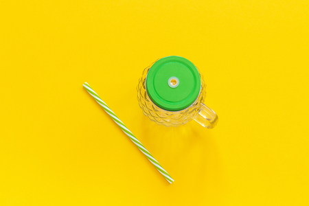 Empty glass jar in form of pineapple with green lid and straw for fruit or vegetable smoothies, cocktails and other beverages on yellow background. Top view Copy space Template.の写真素材