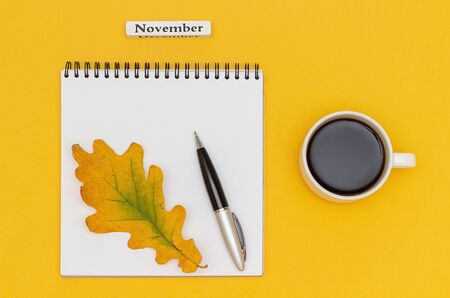 Autumn composition. Text November Coffee Cup, open notepad with pen and yellow oak leaf on yellow paper background. Top view Flat lay Mockup.の写真素材