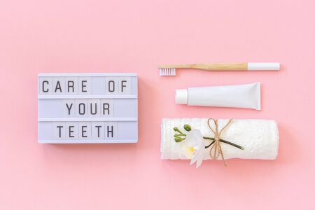 Care of your teeth text on light box and natural eco-friendly bamboo brush for teeth, towel, toothpaste tube. Set for washing on pink background. Concept dental health care Top view.の写真素材