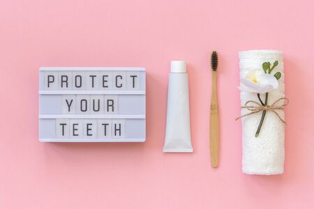Protect your teeth text on light box and natural eco-friendly bamboo brush for teeth, towel, toothpaste tube. Set for washing on pink background. Concept dental health care Top view.の写真素材