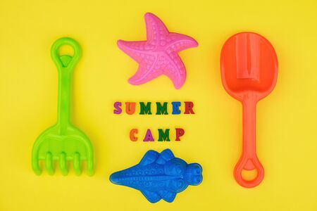Text Summer camp and multicolored set children's toys for summer games in sandbox or on sandy beach on yellow background. Creative top view Flat lay Concept children's rest and development.の写真素材