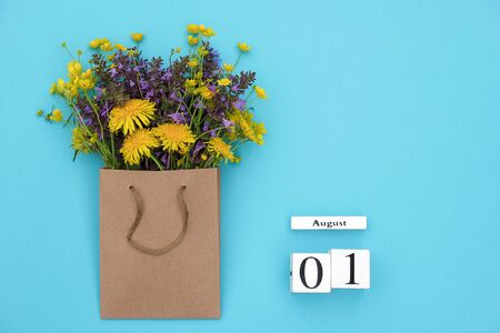 Wooden cubes calendar August 1 and field colorful rustic flowers in craft package on blue background. Greeting card Flat Lay Concept Hello August Template with copy space for text and design.の写真素材