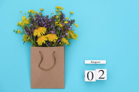 Wooden cubes calendar August 2 and field colorful rustic flowers in craft package on blue background. Greeting card Flat Lay Concept Hello August Template with copy space for text and design.の写真素材