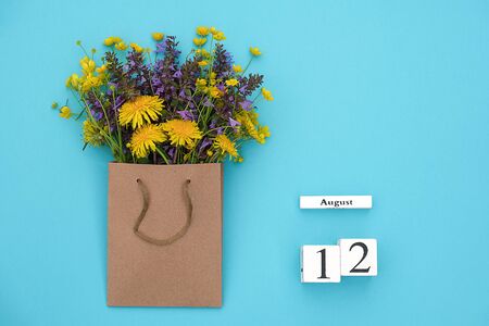 Wooden cubes calendar August 12 and field colorful rustic flowers in craft package on blue background. Greeting card Flat Lay Concept Hello August Template with copy space for text and design.の写真素材