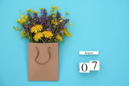 Wooden cubes calendar August 7 and field colorful rustic flowers in craft package on blue background. Greeting card Flat Lay Concept Hello August Template with copy space for text and design.の写真素材