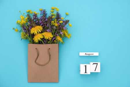 Wooden cubes calendar August 17 and field colorful rustic flowers in craft package on blue background. Greeting card Flat Lay Concept Hello August Template with copy space for text and design.の写真素材