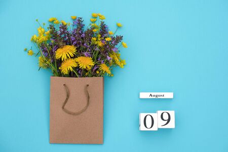 Wooden cubes calendar August 9 and field colorful rustic flowers in craft package on blue background. Greeting card Flat Lay Concept Hello August Template with copy space for text and design.の写真素材