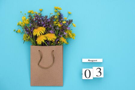 Wooden cubes calendar August 3 and field colorful rustic flowers in craft package on blue background. Greeting card Flat Lay Concept Hello August Template with copy space for text and design.の写真素材