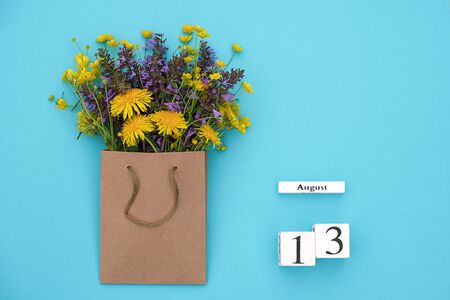 Wooden cubes calendar August 13 and field colorful rustic flowers in craft package on blue background. Greeting card Flat Lay Concept Hello August Template with copy space for text and design.の写真素材