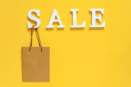 Text SALE from white volume letters and blank shopping bag on yellow background. Top view Flat lay Copy space Concept discount. Creative template for your text, design, ad or advertisement.の写真素材