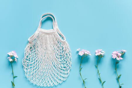 Delicate flowers and white reusable shopping eco mesh bag on blue background. Concept no plastic, zero waste and caring for environment. Copy space Top view Layout for your design.の写真素材