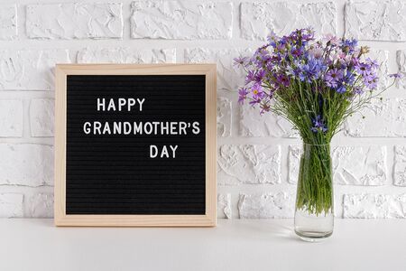 Happy grandmothers day text on black letter board and bouquet blue flowers in vase on table against white brick wall. Concept Mothers Day. Template for greeting card, postcard.の写真素材