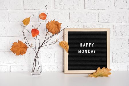 Happy Monday text on black letter board and bouquet of branches with yellow leaves on clothespins in vase on table Template for postcard, greeting card Concept Hello autumn Monday.の写真素材