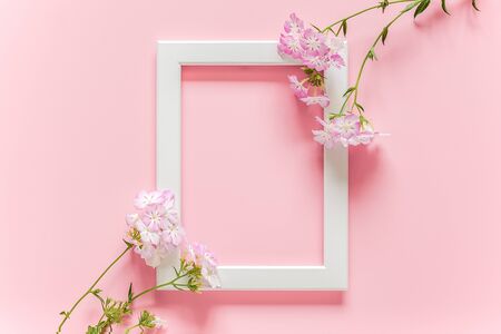 White wooden picture frame and flowers on pink background with copy space. Creative Top view Flat lay Mock up Template for invitstion, greeting card.の写真素材