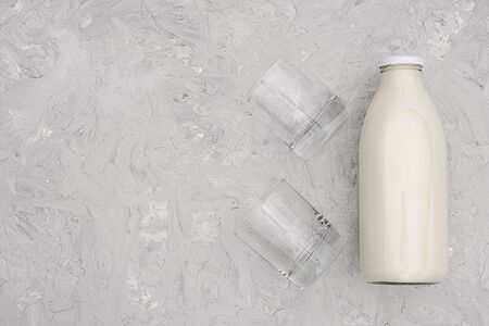 Milk in glass bottle and two empty glasses on gray background with copy space. Flat lay top view,