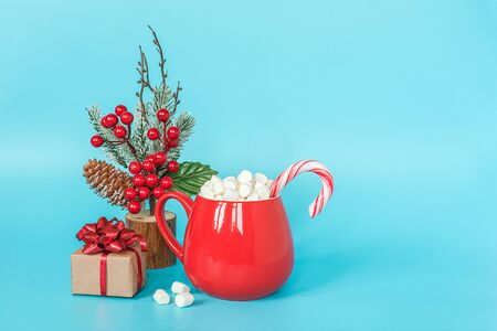 Gift box, christmas decoration and red cup of marshmallows with lollipop cane on blue background. Merry Christmas or Happy New Year concept. Copy space Template for your design, Greeting card.の写真素材