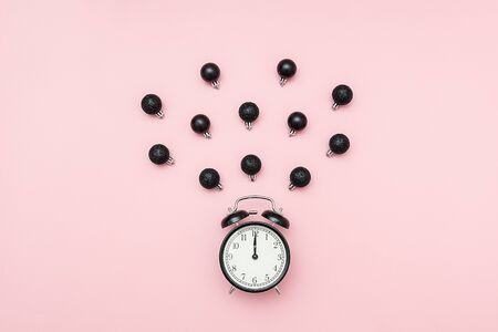 Christmas or New year midnight concept. Black alarm clock and flying christmas decor black baubles on pink background. Creative flat lay, top view, template for yuor design, greeting card, invitation.の写真素材