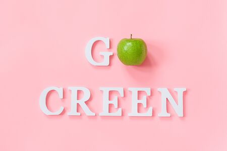 Go green concept. Green natural fresh apple and text Go green from white letters on pink background. Creative flat lay Top view Copy space.の写真素材
