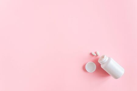 White medical bottle and two pills dietary supplements, nutraceuticals, antibiotic, painkillers on pink background. Health and drug treatment concept. Top View Copy Space.の写真素材