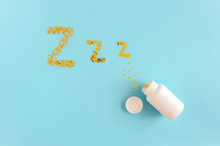 Gold stars confetti fly out white bottle in form of dream symbols Z Z Z on blue background. Concept Insomnia, sleep problems and sleeping pill. Top view Flat lay Copy space.の写真素材