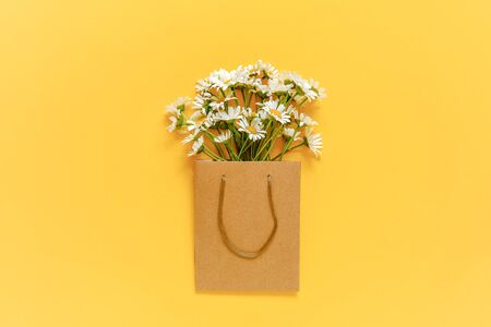 Field chamomiles flowers in craft package on yellow background. Greeting card Flat Lay Copy space. Good day Template for text and designの写真素材