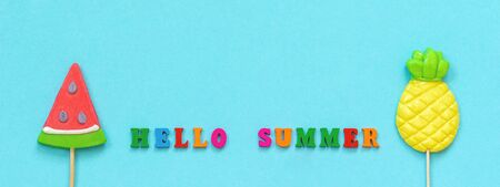 Hello summer colorful text, pineapple and watermelon lollipops on stick on blue paper background. Concept vacation or holidays Creative Top view Copy space Template Greeting card, postcard.の写真素材