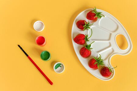 Red ripe strawberries on an artistic palette, brush and gouache on yellow background with copy space. Creative concept summer colors paint. Top view Flat lay Template for design postcard invitation.の写真素材