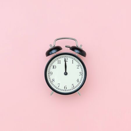 Black alarm clock in center on pink background, closeup. Minimal style Copy space Top view Template...