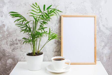 Wooden vertical frame with white blank card, cup of coffee and green exotic palm flower in pot on table on gray concrete wall background. Mockup Template for your design, text.の写真素材