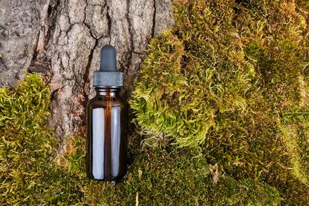 One brown glass bottles and pipette whith serum, essential oil on green moss and tree bark background. Natural Organic Spa Cosmetic concept.の写真素材