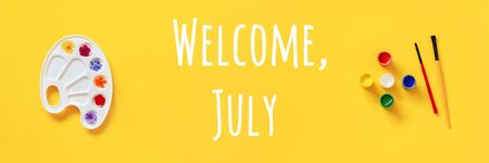 Welcome July text. Colorful flowers on artistic palette, brush, gouache on yellow background. Creative concept Hello summer. Top view Flat lay Banner.の写真素材
