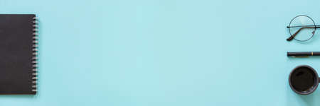 Office or home workplace. Black color notepad, cup of coffee, spectacles, pen on blue background....