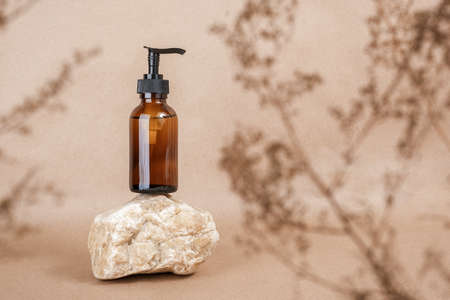 Brown glass bottle with pump of cosmetic products on stone framed by dried plant flowers on beige craft paper background. Natural Organic Spa Cosmetic Beauty concept Front view Mock up.の写真素材