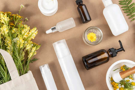 Various bottles, tubes, jar with cosmetic, wildflowers in eco textile bag, mortar bowl with pestle on beige background. Concept natural herbal organic cosmetic, homeopathic cosmetology. Top view.の写真素材