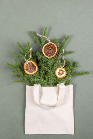 A bouquet of fir branches with circles of dried oranges in fabric eco bag on green background....