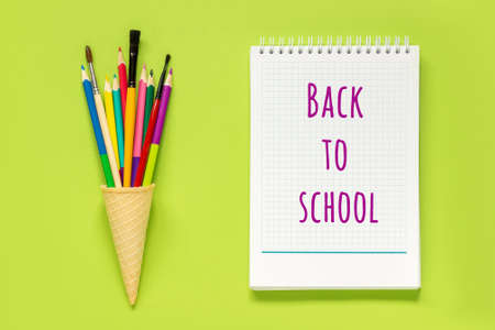 Back to school text on white notepad and colored pencils in waffle ice cream cone on green...
