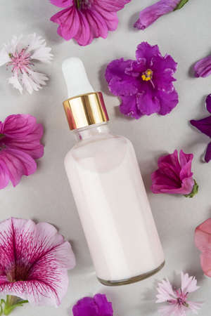 Pink anti-aging collagen, facial serum or other cosmetic product in glass bottle among the purple flowers on gray background. Natural Organic Spa Cosmetic concept Mockup Top view.の写真素材