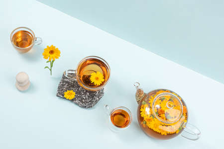Cup of herbal tea and transparent teapot with calendula flowers on blue background. Calendula Tea Benefits Your Health concept. Top view Flat lay.の写真素材