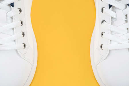 Two white sports shoes, sneakers with shoelaces on the edges of the yellow background with copy space. Sport lifestyle concept Top view Flat lay Close-up.の写真素材
