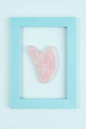 Massage tool jade Gua sha from crystal rose quartz in frame on blue background. Facial anti-age massage for natural lifting and toning treatment at home. Beauty concept Top view.の写真素材