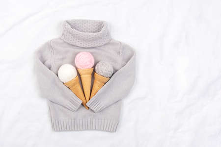 Three ice cream from ball of yarn in waffle cones and gray knitted sweater on white background. Top...