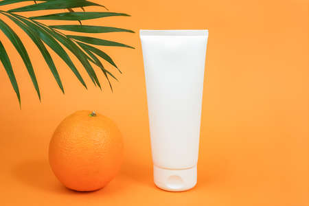 White blank cosmetic bottle, tube of cream, lotion for body, face or hand, orange fruit and branch of palm. Concept cosmetics with vitamin C, antioxidants or anti-cellulite. Mockup Front view.の写真素材