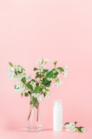 One white blank cosmetic tube bottle and flower, blooming branch on pink background. Natural Organic Spa Cosmetic Beauty Concept. Mockup Front view.の写真素材