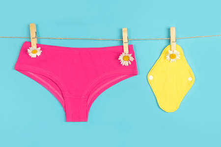 Yellow eco reusable menstrual pads and pink panties with chamomile flowers on washing line, blue background. Health care and zero-waste, no plastic, eco-friendly concept.の写真素材