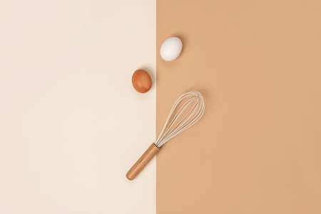 Two brown Eggs and whisk with wooden handle on beige background. Flat lay Top view Concept.