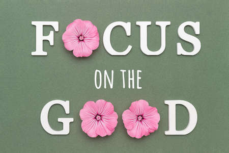 Focus on the good. Motivational quote from white letters and pink flowers on green background. Creative concept inspirational quote of the day.の写真素材