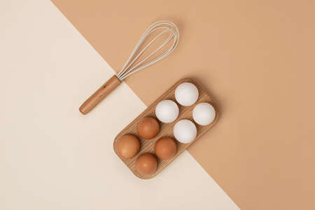 Eggs in wooden egg box and whisk on beige brown background. Flat lay Top view Copy spaceの写真素材