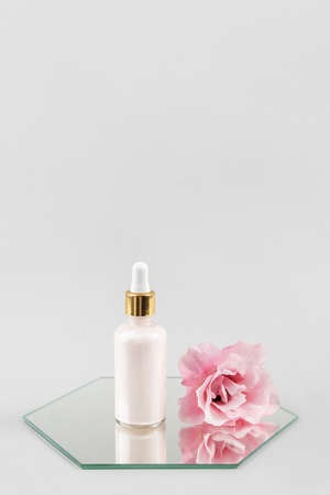 One glass dropper bottle with serum, essential oil or other cosmetic product and beautiful pink flowers on mirror on gray background. Natural Organic Spa Cosmetic Beauty concept. copyspace.の写真素材